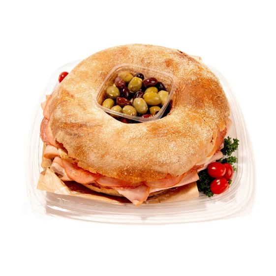 Ring-shaped muffaletta sandwich tray with deli meats, cheese, central olive mix, and cherry tomatoes garnish.